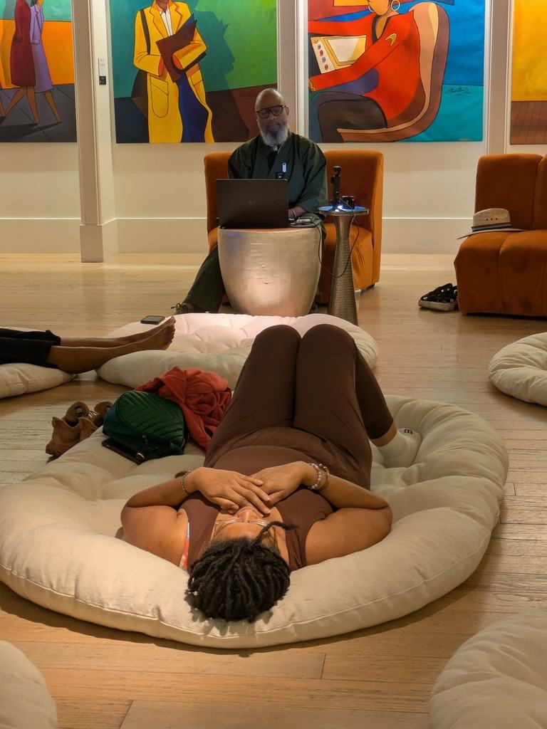 Heru TchaasAmen leading a guided rest practice with a participant resting on a floor cushion