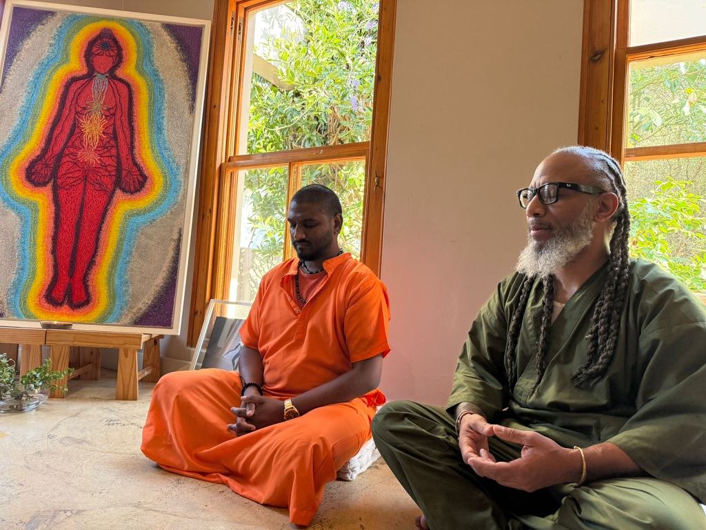 Heru TchaasAmen meditating in Johannesburg, South Africa, beside an energy body painting