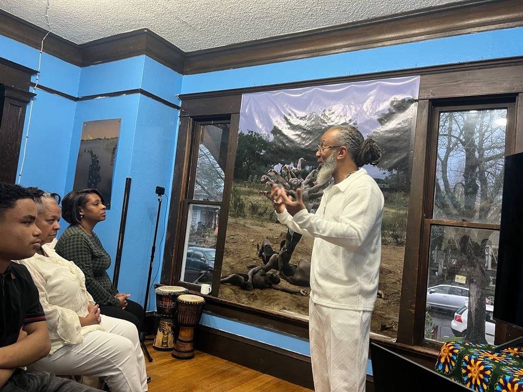 Heru TchaasAmen teaching at Wa Na Wari in a room with djembe drums