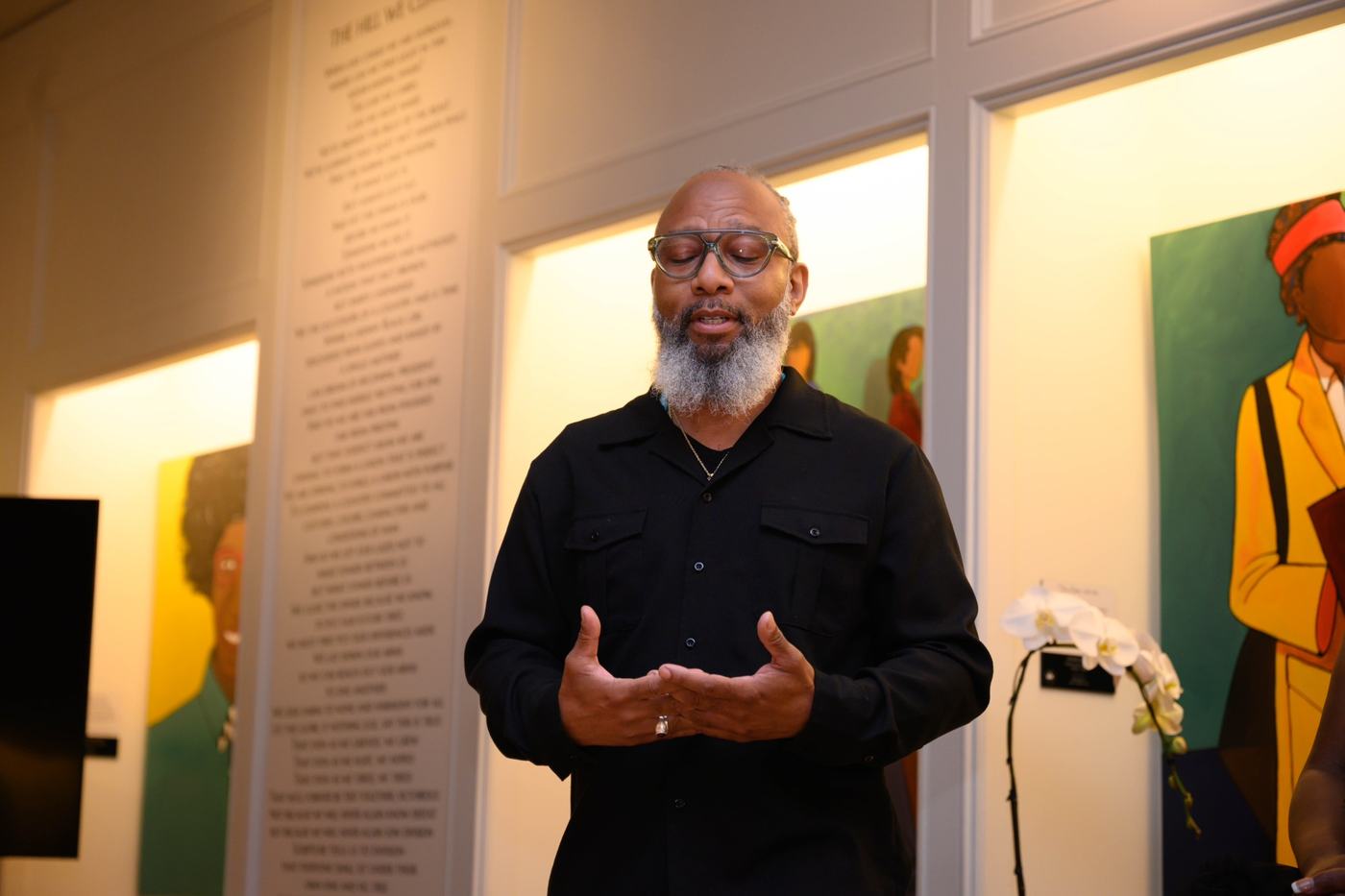 Heru TchaasAmen speaking beside The Hill We Climb text installation at WOW Gallery