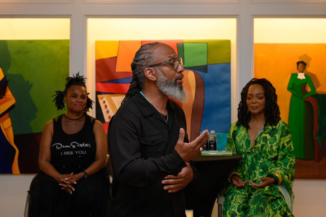 Heru TchaasAmen speaking at WOW Gallery with vibrant painted portraits behind him